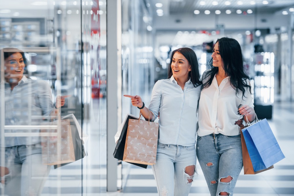 Two young women holding shopping bags in a mall.