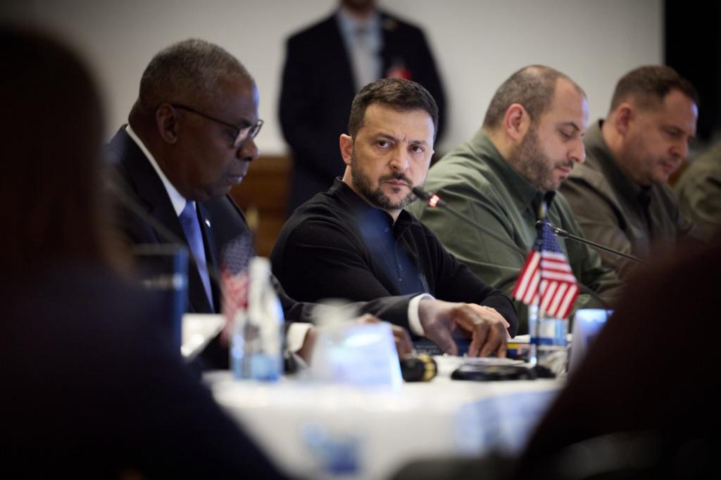 Ukrainian President Volodymyr Zelensky sitting at a table with other men and next to US Defense Secretary Lloyd Austin, during a summit at the Ramstein air base in Germany, discussing military support