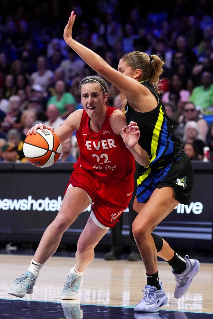 Caitlin Clark #22 of the Indiana Fever in action, driving against Jacy Sheldon #4 of the Dallas Wings in a basketball game.