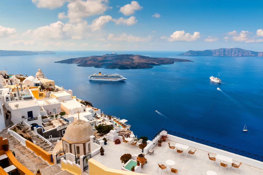 Wide angle view of cliff-side buildings in Santorini, Greece with large cruise ships in the water.