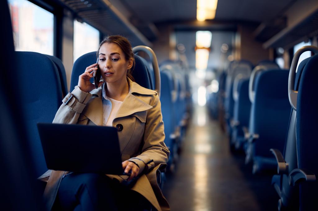 Young businesswoman using laptop and talking on phone while commuting on a train