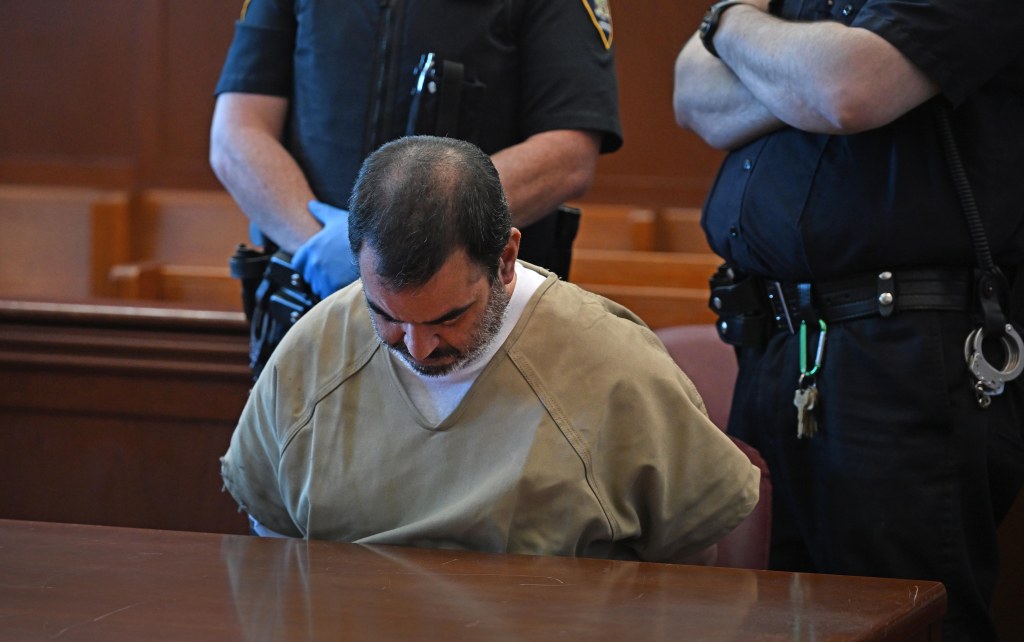 Edward Asencio sitting head down during his arraignment at a Manhattan court table with police officers behind him