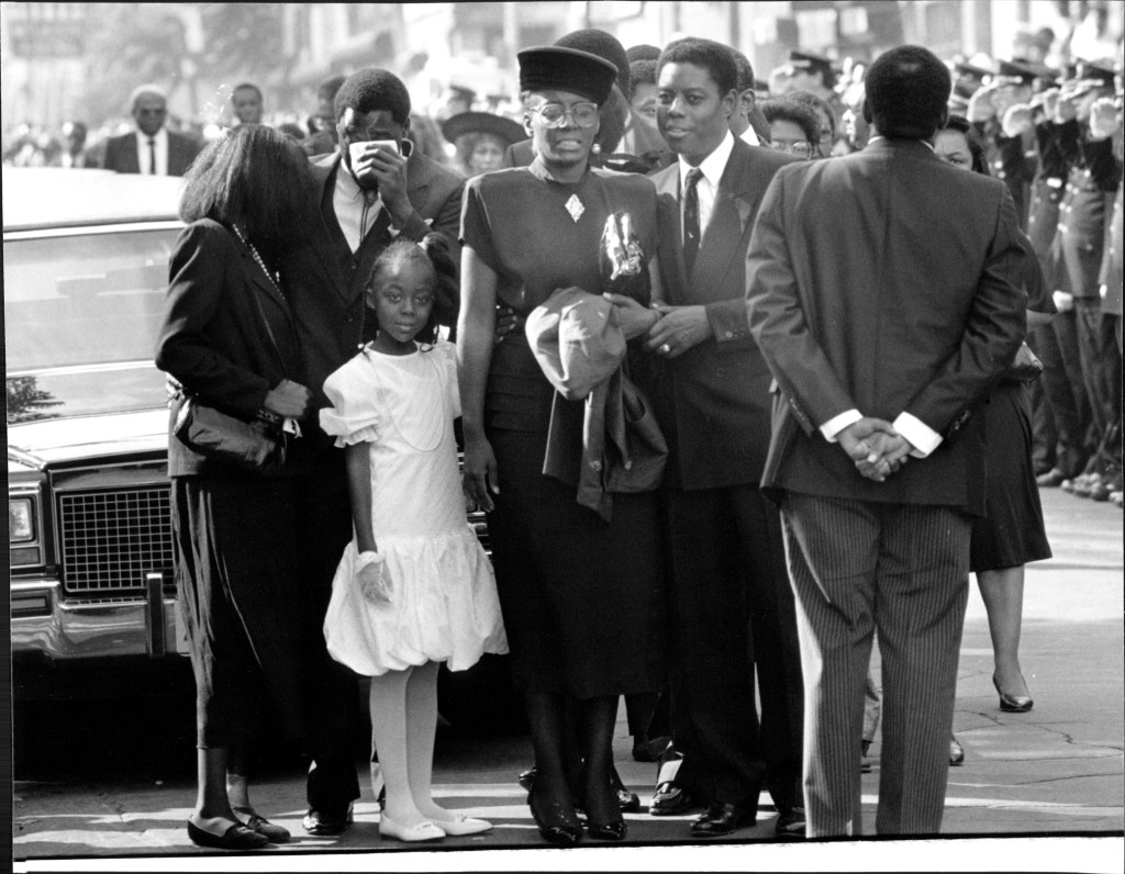 The police officer's daughter wearing a white dress and gloves at her dad's funeral.