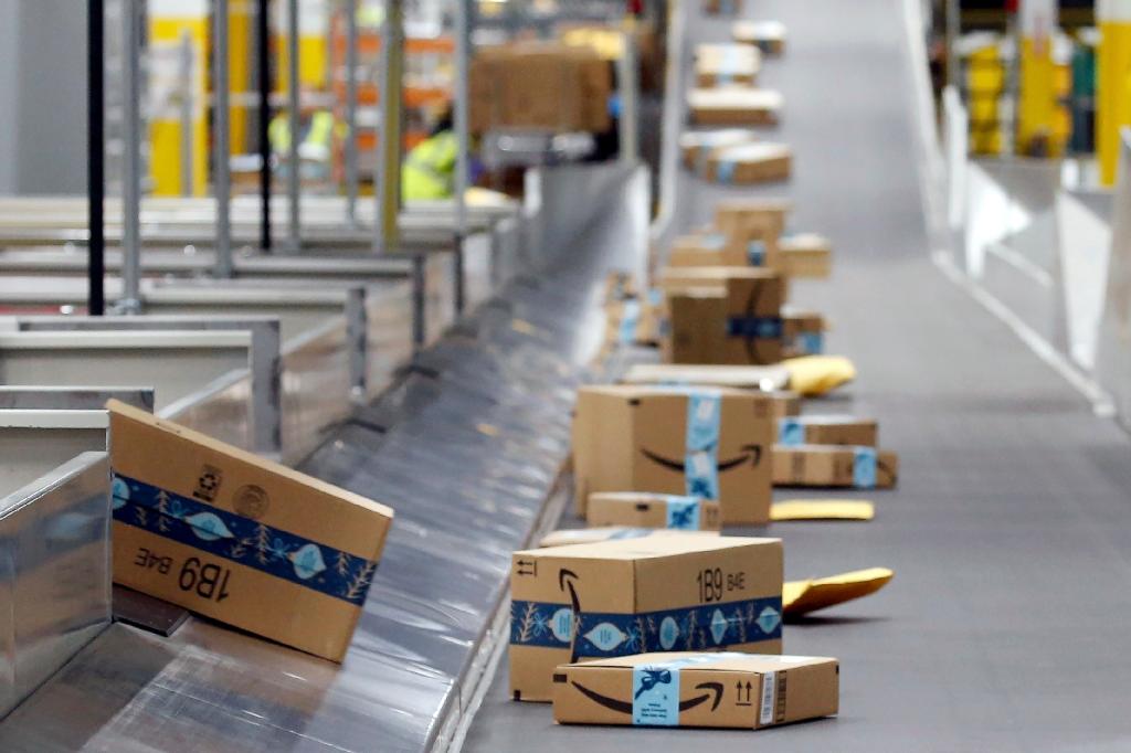 Amazon packages move along conveyer belt at warehouse.