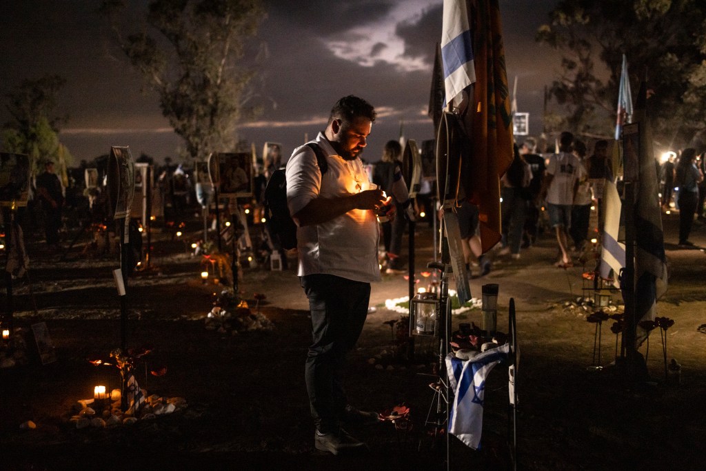 A man lighting a candle during a memorial ceremony for Israelis killed in the October 7 Hamas attack, surrounded by attendees at the Nova memorial near Kibbutz Reim