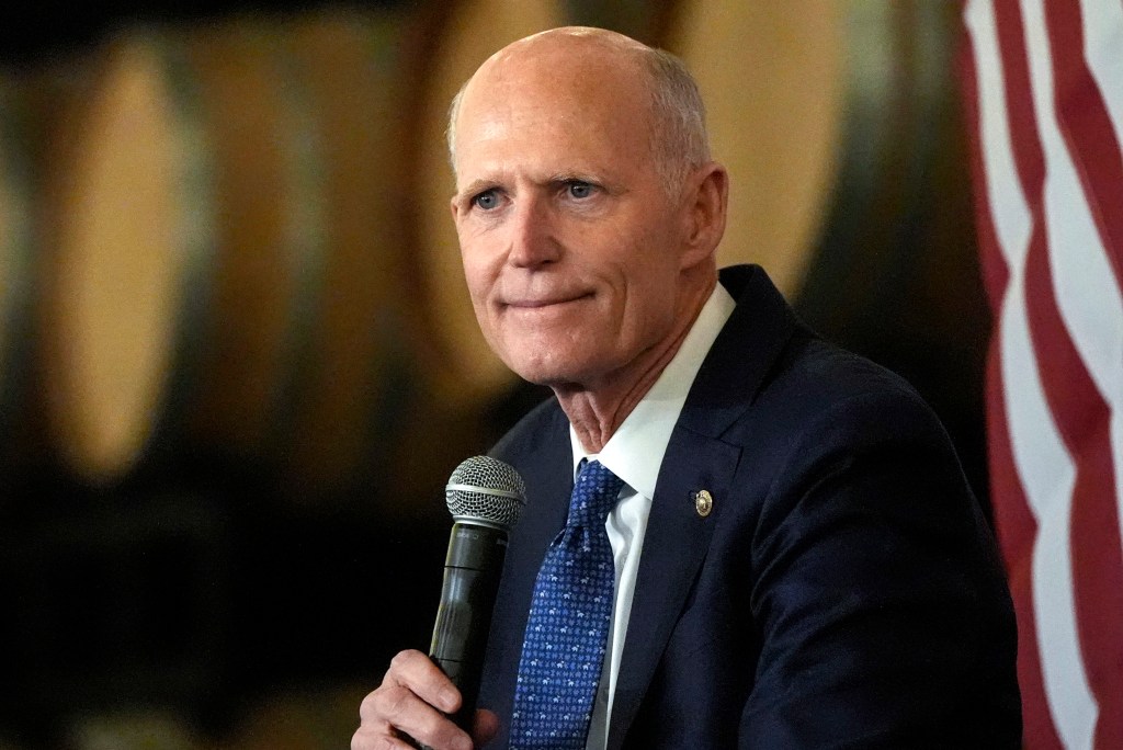 Senator Rick Scott speaking at a town-hall meeting in Braselton, Georgia, in 2024, holding a microphone in support of Republican policies