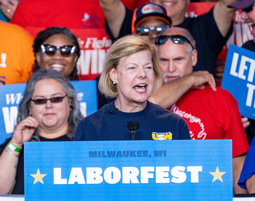 U.S. Senator Tammy Baldwin speaking into a microphone at Laborfest 2024, pointing to highlight a point in her remarks