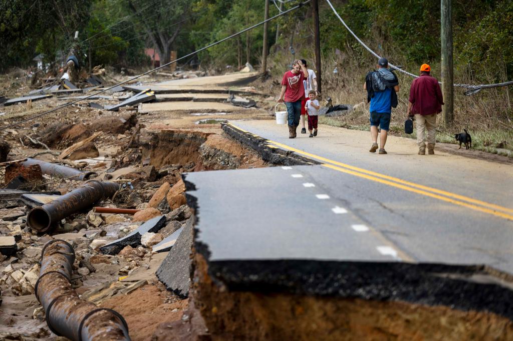 Swannanoa residents walking through devastating flood damage caused by the remnants of Hurricane Helene, with downed trees and power outage in the background