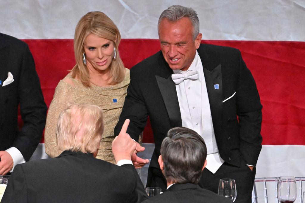 President Trump giving a speech at the Al Smith Dinner, attended by several notable figures including Robert F. Kennedy Jr. and Cheryl Hines, with guests sitting around tables.