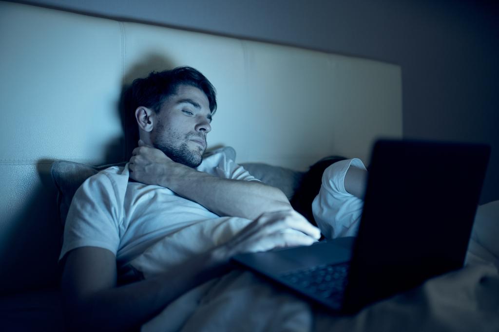 A man on his laptop while wife sleeps. 