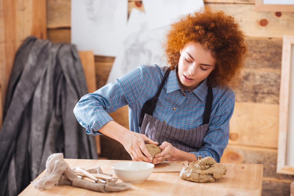 Young redhead woman kneading clay and creating dishes in a pottery studio