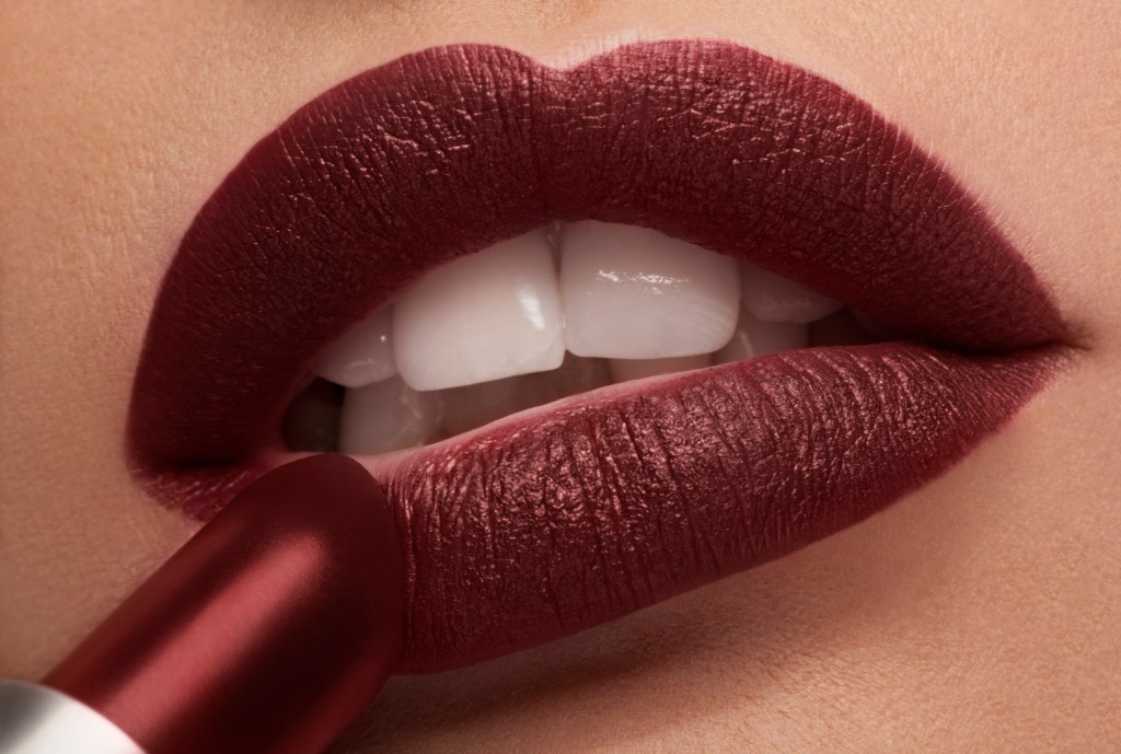 Close up image of a woman applying red lipstick under studio lighting