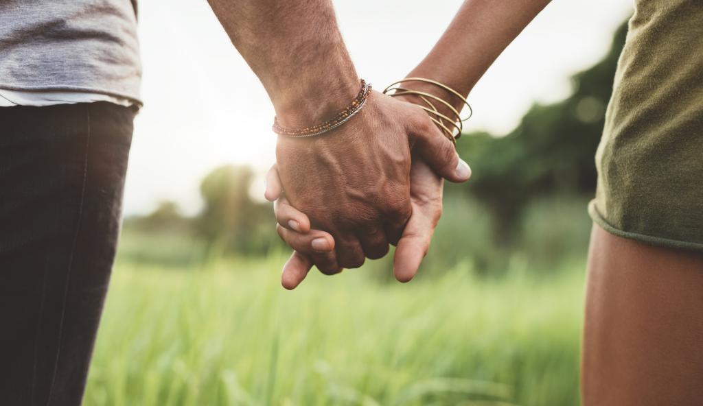 Young couple walking hand in hand through a meadow, with a close up view of their entwined hands