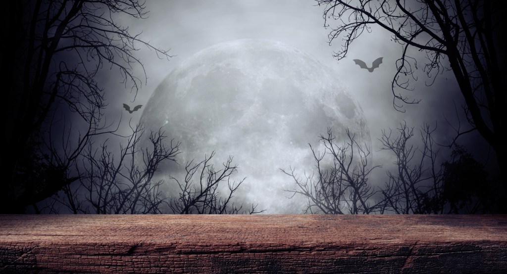 Old wooden table under a full supermoon with silhouette of a dead tree and bats for Halloween theme