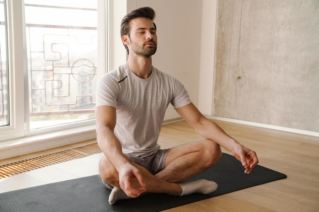 Athletic man focusing and meditating on a yoga mat at home after workout