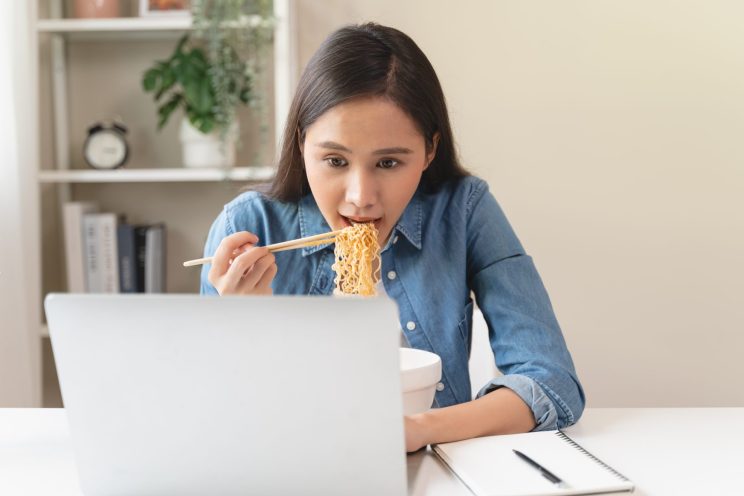 Young female eating instant noodle isolated on background.