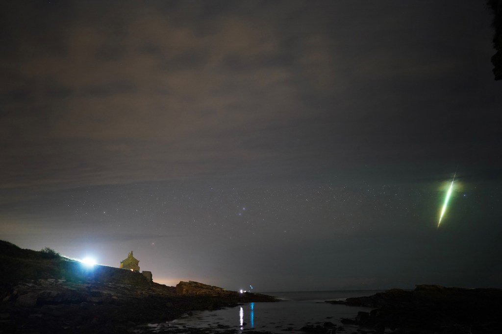 A fisherman observing the Draconid meteor shower over Howick rocks in Northumberland at night.