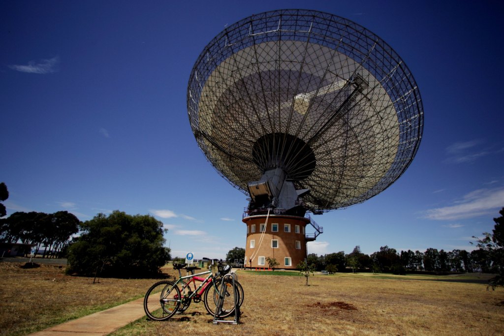 Large radio telescope known as 'The Dish' at the CSIRO’s Australia Telescope National Facility, Parkes Observatory, Australia, pointing to the sky with bicycles in the background