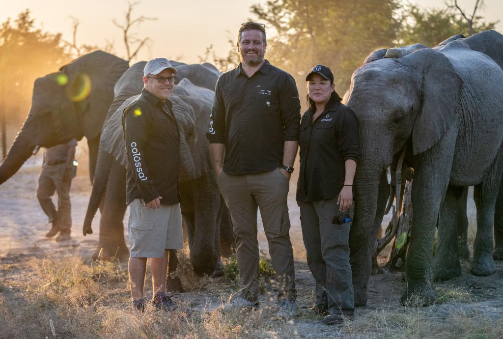 Colossal Biosciences team members Steve Metzler, Matt James and Wendy Kiso standing beside elephants, are planning to resurrect the woolly mammoth by 2028.