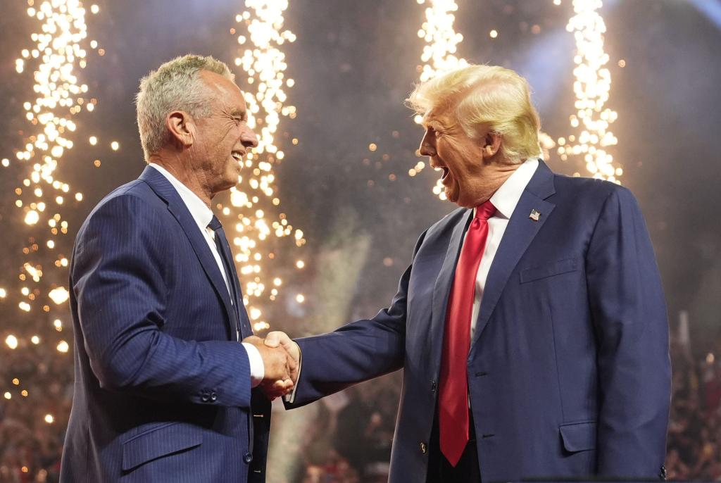 Former President Donald Trump shaking hands with Robert F. Kennedy Jr. on a stage with fireworks in the background at a campaign rally in Glendale, Arizona, 2024