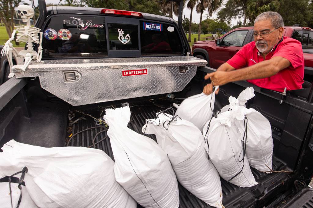 Man, Andrew Samaniego, loading sand bags into pickup truck with skeleton decoration, preparing for Hurricane Milton