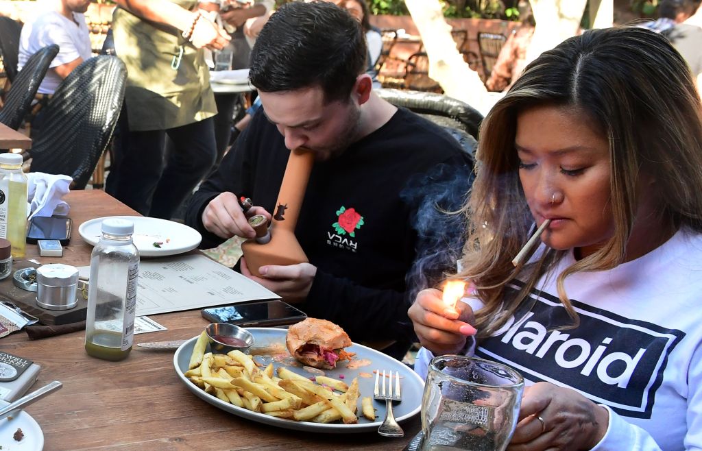 Will Halverson smoking from a bong while Mimi Bui lights a joint with their meal at Lowell Cafe in West Hollywood, California