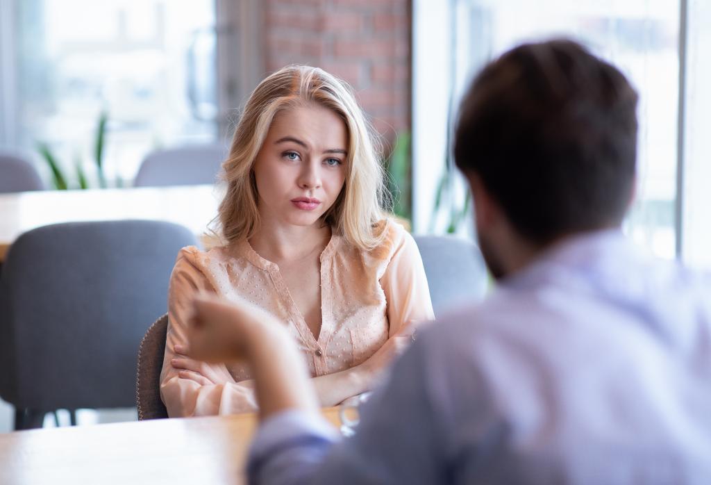 Young woman looking bored and unhappy during a date at a cafe, sitting with arms crossed at table