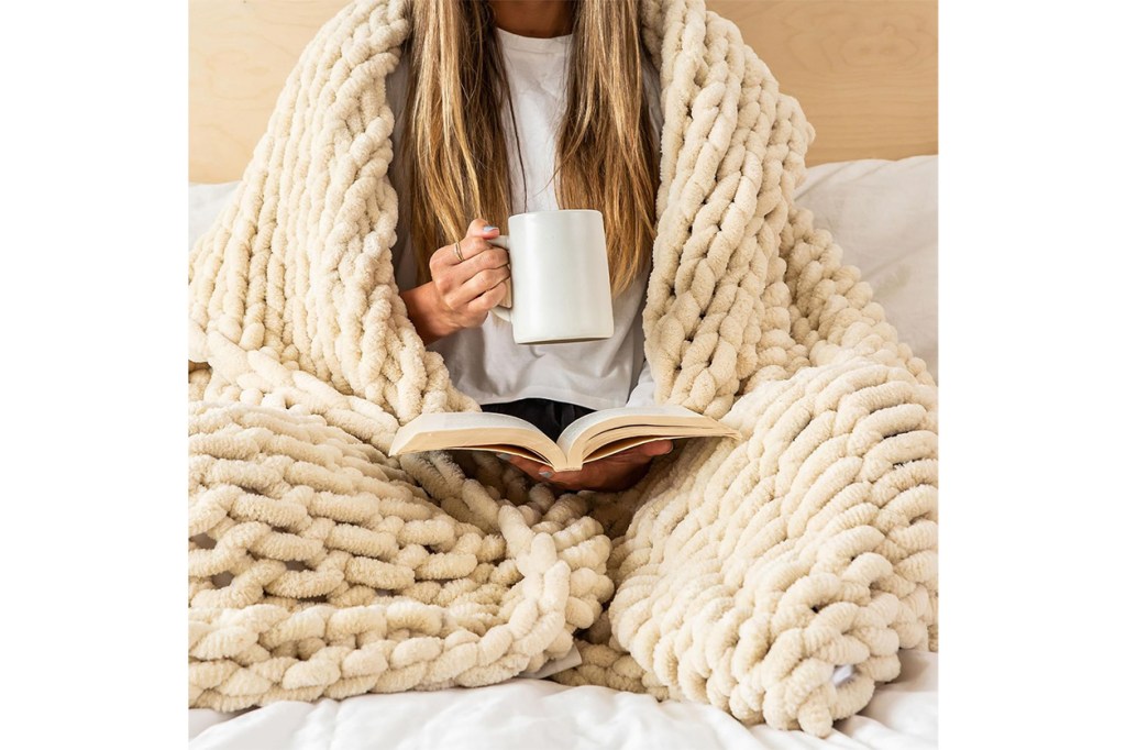 A person sitting on a bed, covered with a blanket, reading a book