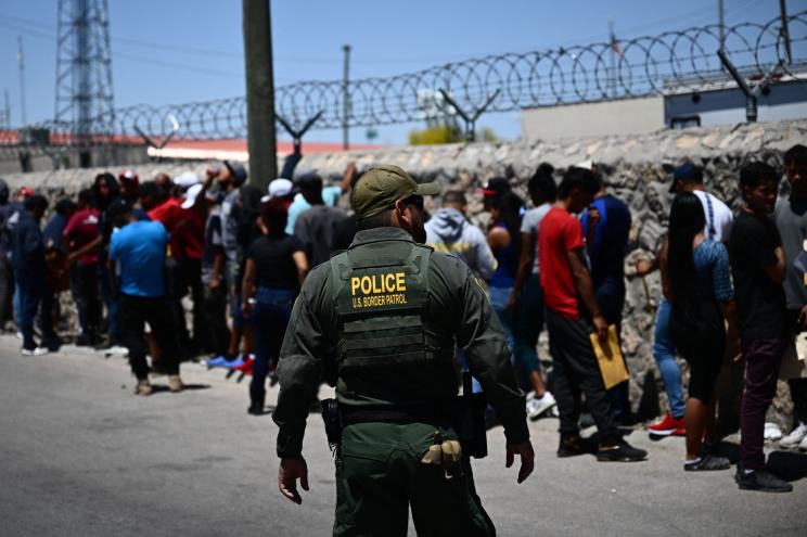 Border Patrol agent walking along a line of migrants near Paso del Norte Port of Entry, El Paso, Texas