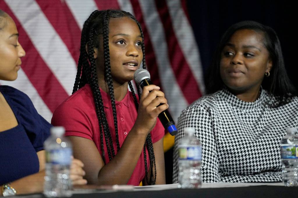 Cynthia Dunlap, an 8th grade student, speaking into a microphone about school choice at a campaign event with her mother, Taccarra Bell, watching.