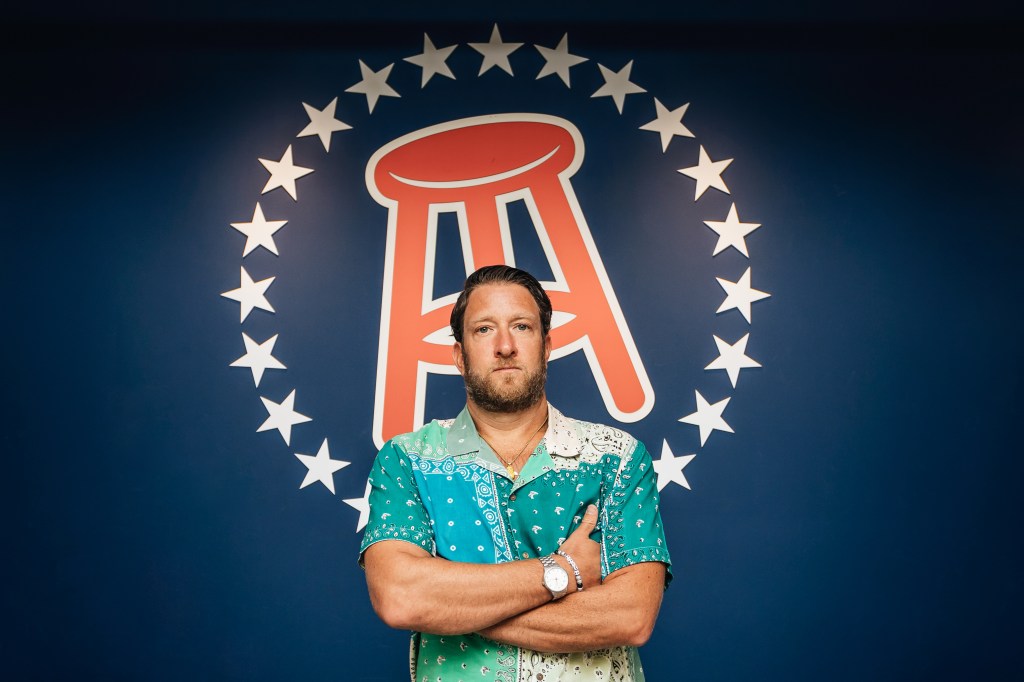 Dave Portnoy with arms crossed in front of Barstool Sports logo.