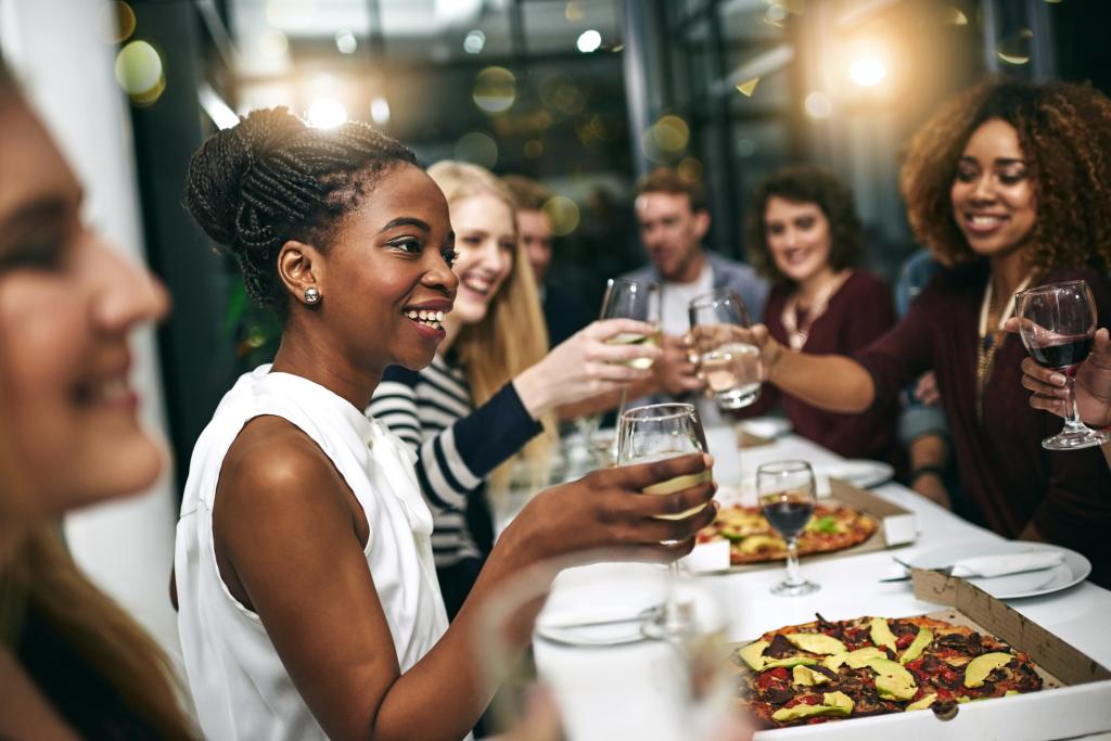 A diverse group of people toasting and celebrating at a dinner party with food and wine