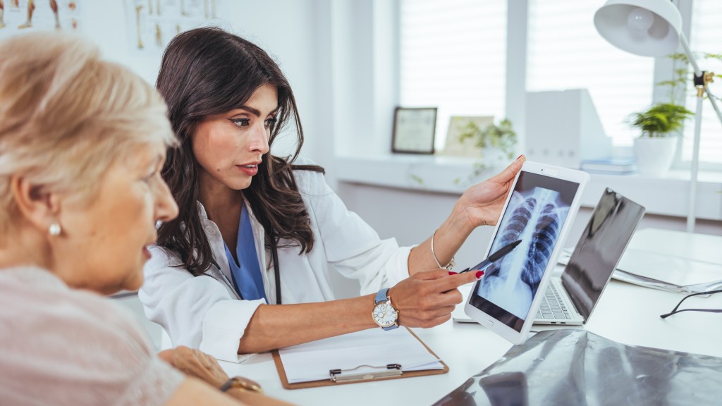 Doctor explaining lung x-ray results on a tablet to an older patient with a cigarette smoking problem in medical clinic