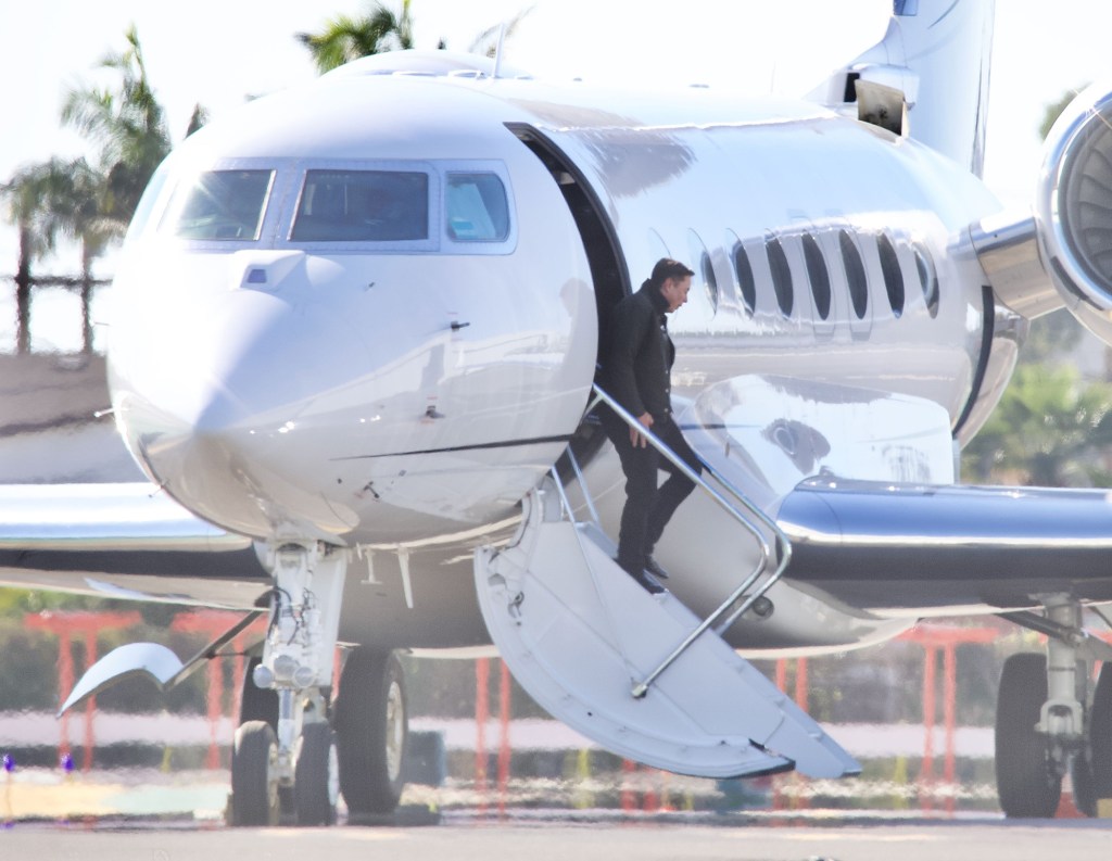 Elon Musk and Natasha Bassett exiting a private jet in Los Angeles, both wearing army green jackets.