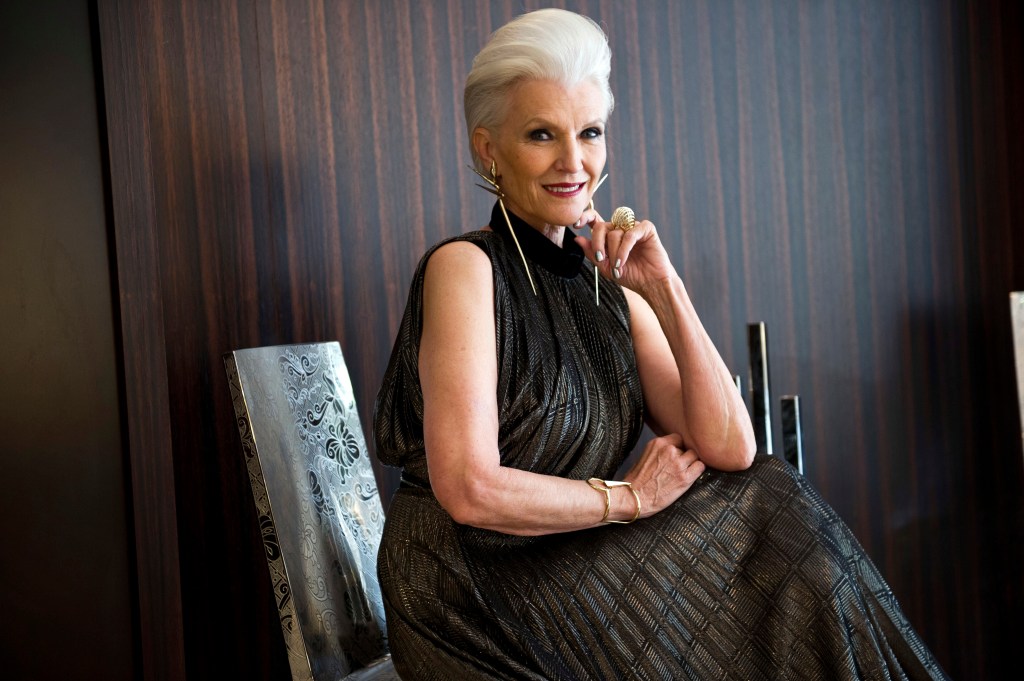 Maye Musk poses in a black gown, seated, smiling