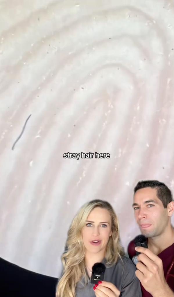 A man and woman doctors examining a magnified image of a dirty hand under a microscope