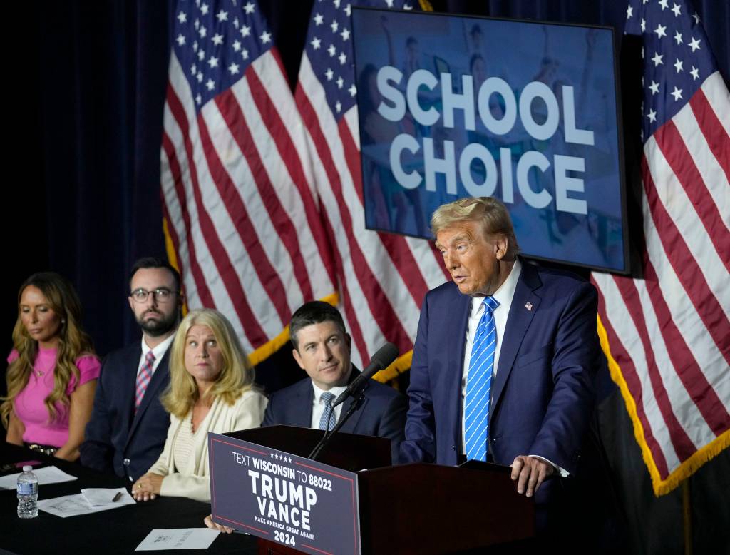 Former President Donald Trump standing at a podium speaking at a campaign event in Discovery World, Milwaukee, with Bryan Steil and other people in the background, on October 1, 2024.