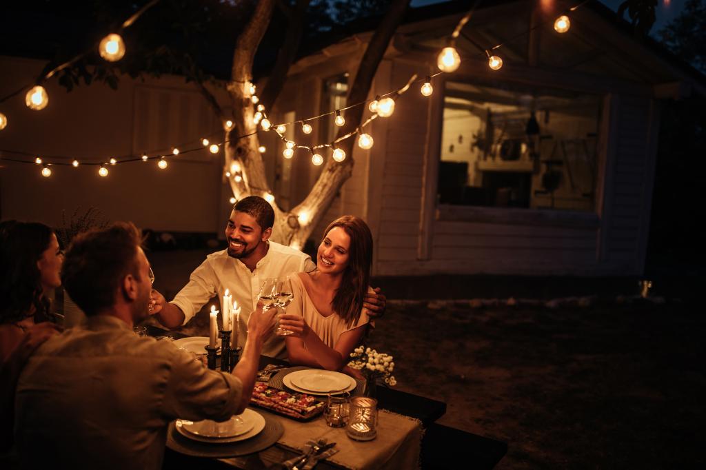 A group of friends enjoying an open-air dinner at a table illuminated by candles