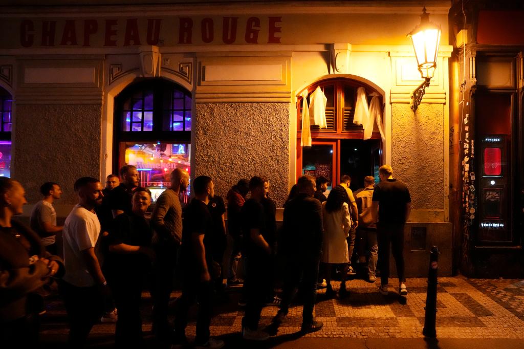 A group of tourists stand in line outside a bar as they attend a pub crawl tour in downtown Prague.