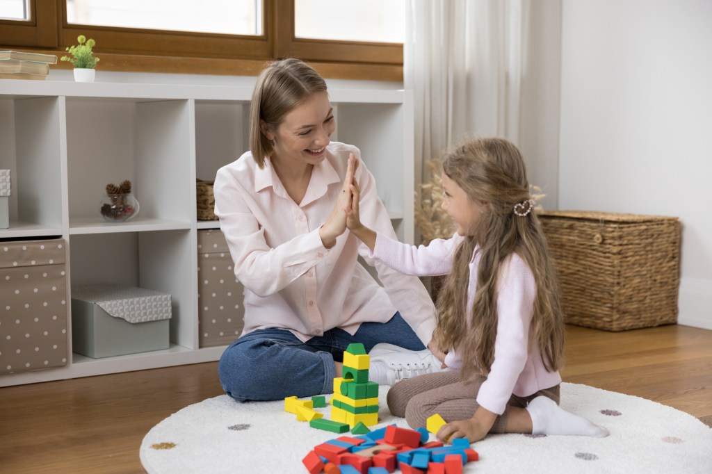 Mom gives high five to daughter while play wooden blocks.