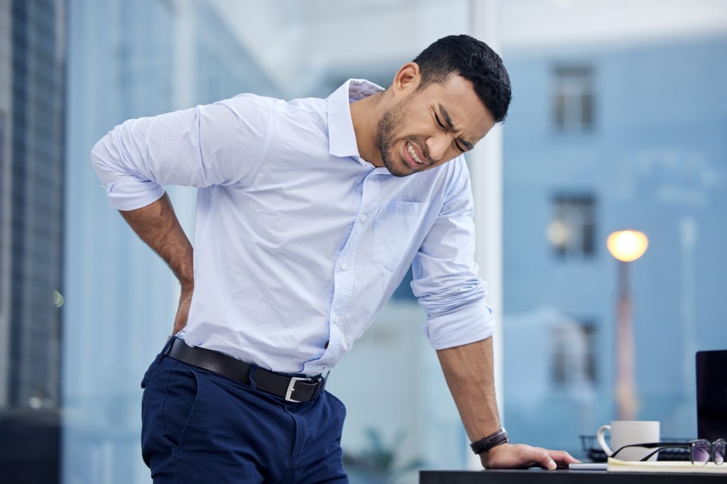 A businessman experiencing backache while standing near his desk at work