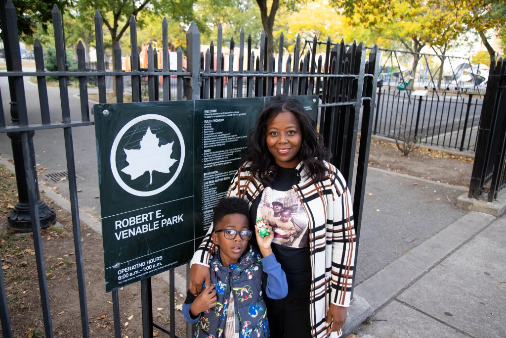 The mother and son next to a sign that says "Robert E. Venable Park" with the swing sets behind them.