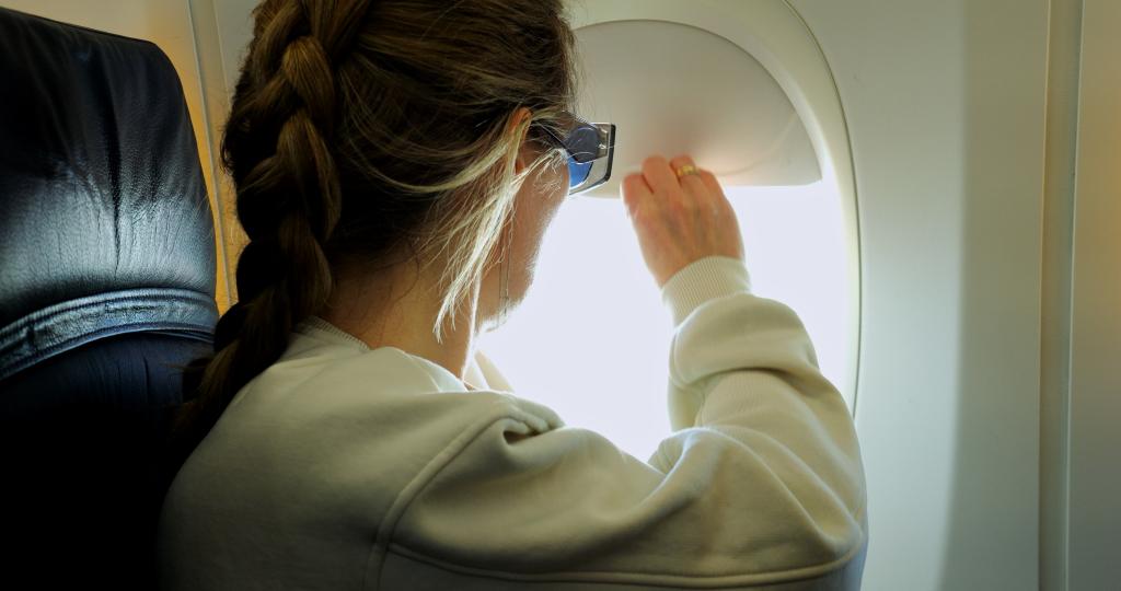 A woman touching an airplane window shade. 