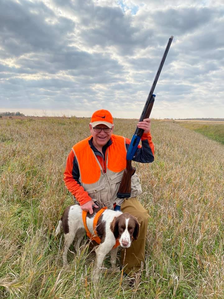 Tim Walz holding a gun next to his dog wearing an orange vest and hat