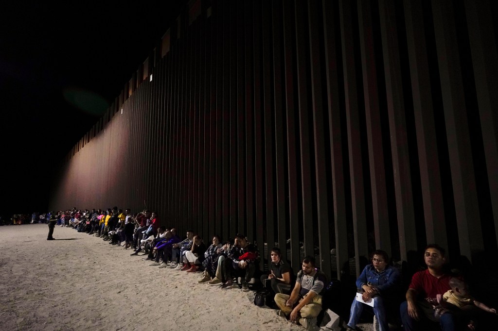 Migrants wait to be processed after crossing into the United States near the end of a border wall, on Aug. 23, 2022, near Yuma, Ariz. (AP Photo/Gregory Bull)