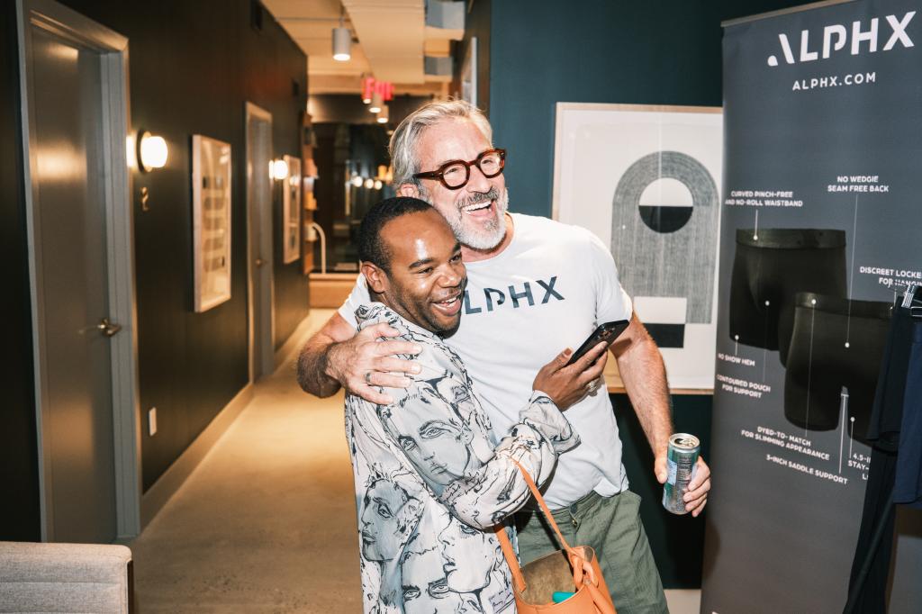 Julian Andrew and Garrett Swann hugging in a hallway at an ALPHX Tupperware party in New York, NY on September 26, 2024