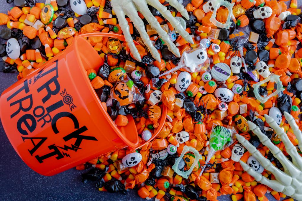 Orange trick or treat bucket spilling various Halloween candies including Skittles and M&M's on a black stone surface