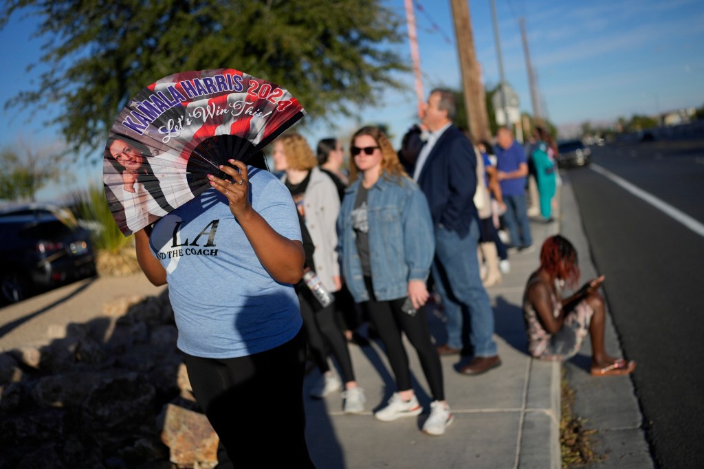 Crowd of people waiting in line to attend a rally where former President Barack Obama is speaking in support of Vice President Kamala Harris, North Las Vegas, Nev., 2024, with a woman holding a fan