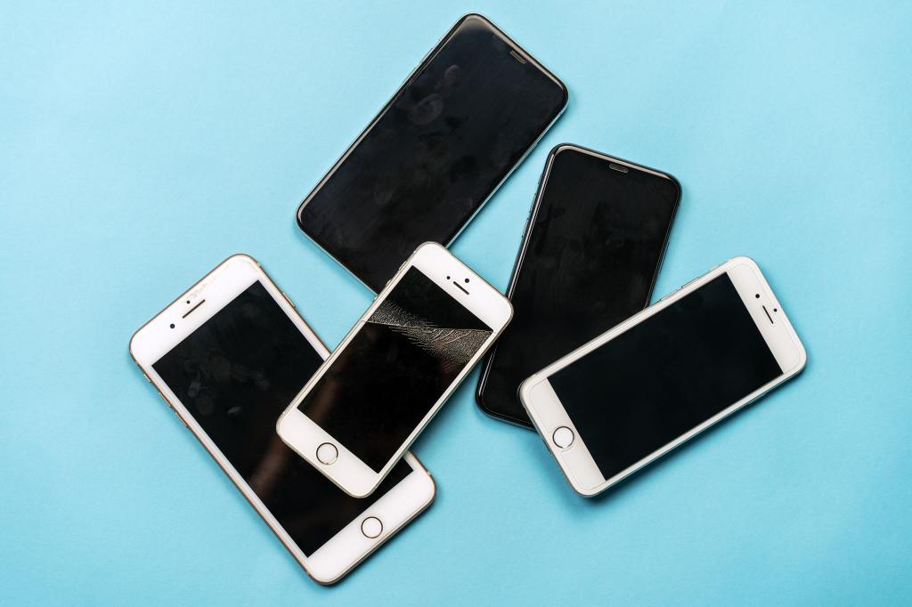 Pile of used, old model black and white mobile phones with dirty finger spots and broken screens on a blue background