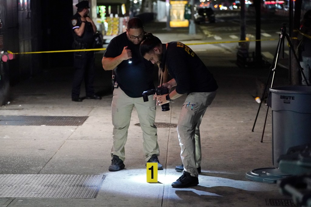 One police officer with a flashlight and the other with a camera pointing down at the sidewalk.